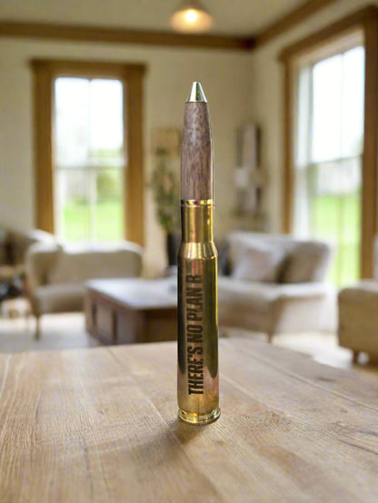 Engraved brass bullet pen standing on a wood table in a sunlit room
