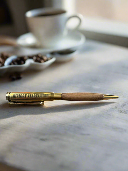 Engraved brass pen beside a coffee cup on a stone counter