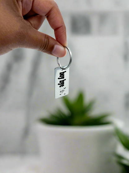 Hand holding a small engraved aluminum keychain