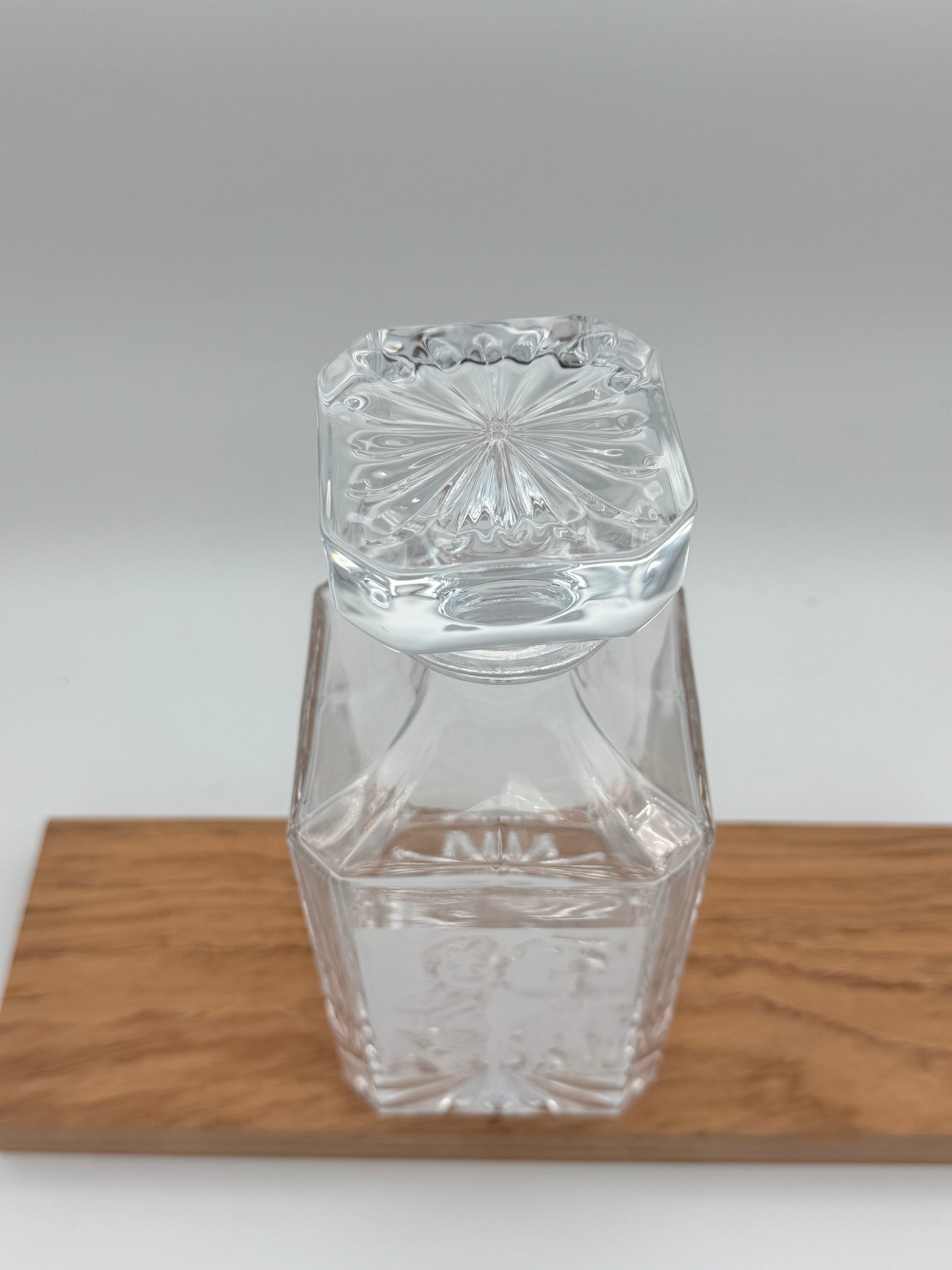 Square glass decanter with stopper, side view on a wood board