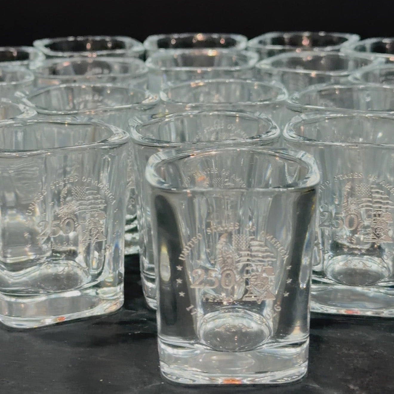 Bulk order of engraved square shot glasses on a dark surface