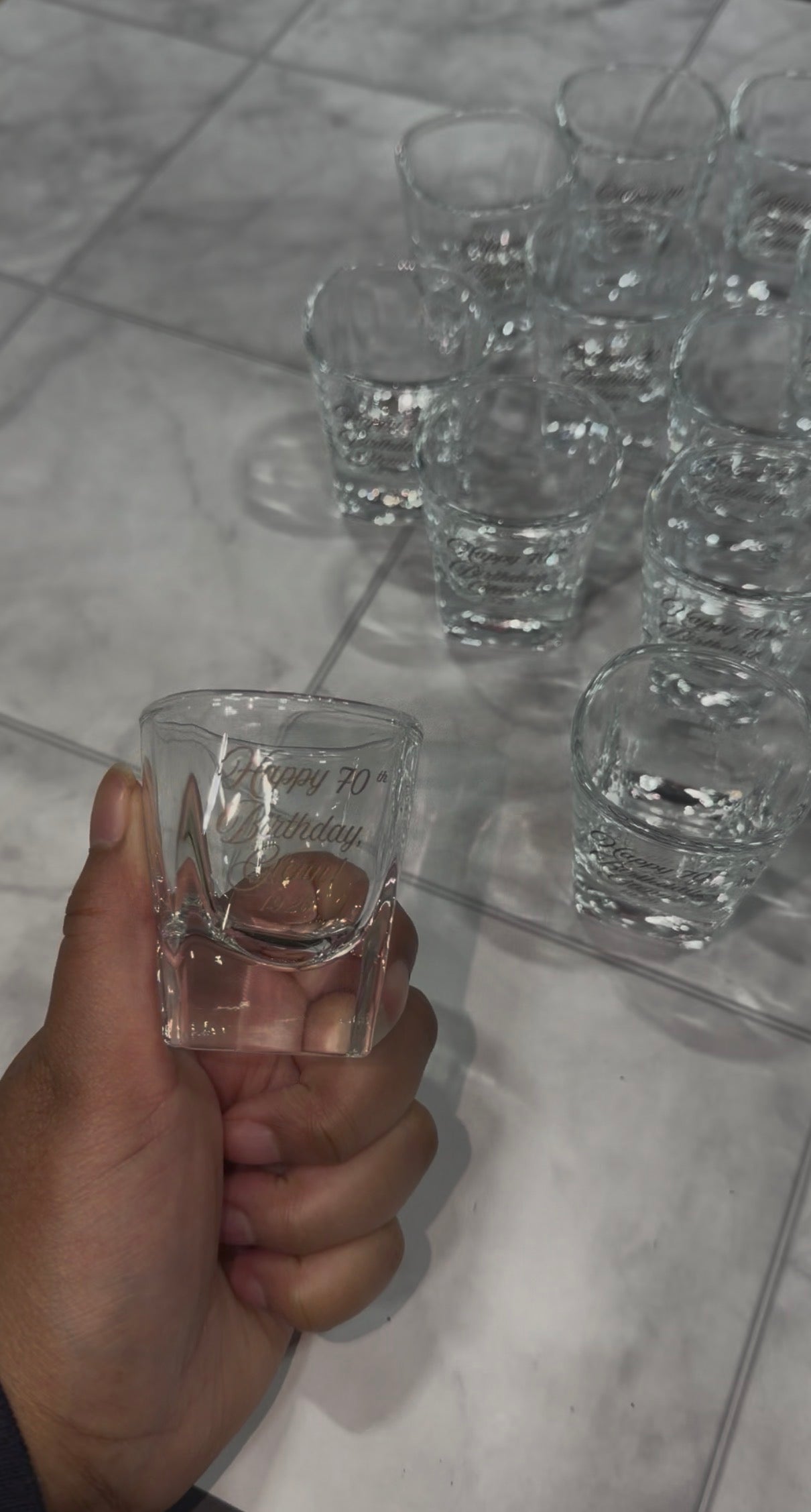 Hand holding an engraved shot glass with a bulk order behind