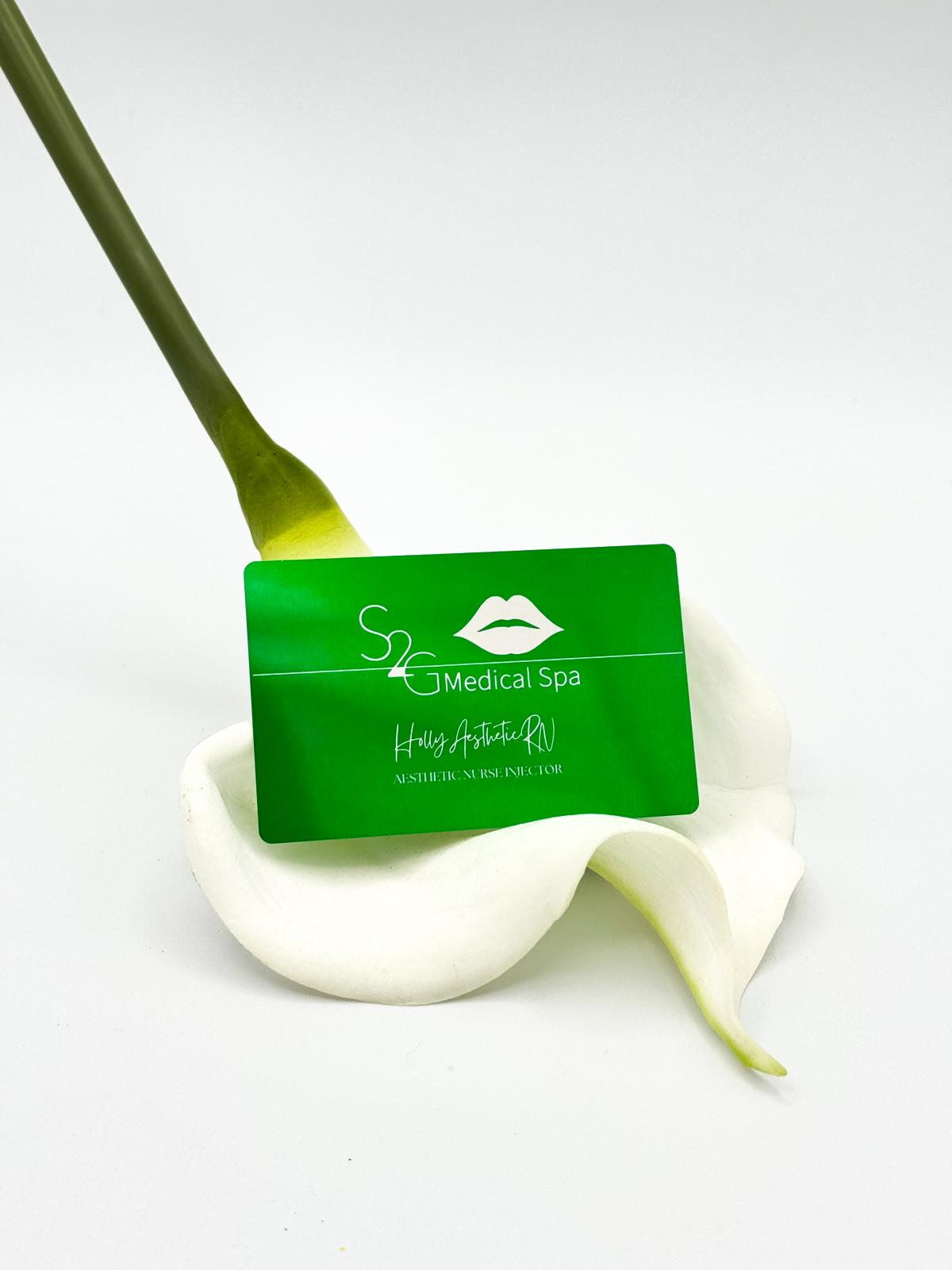 A green rectangular spa card with white logo and text reading 'S2 Medical Spa' and 'Handcrafted in New York City,' placed on a white calla lily against a clean white background.