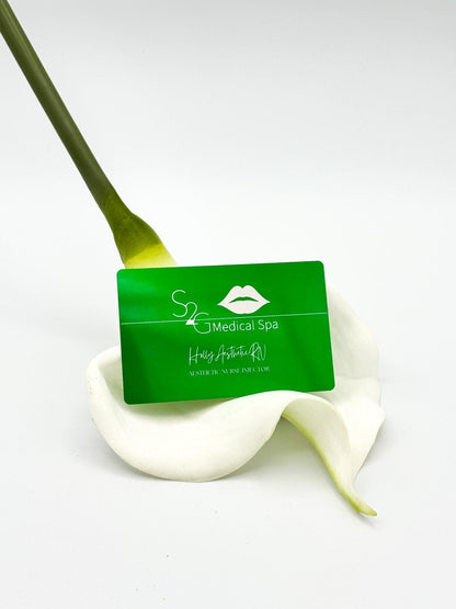 A green rectangular spa card with white logo and text reading 'S2 Medical Spa' and 'Handcrafted in New York City,' placed on a white calla lily against a clean white background.
