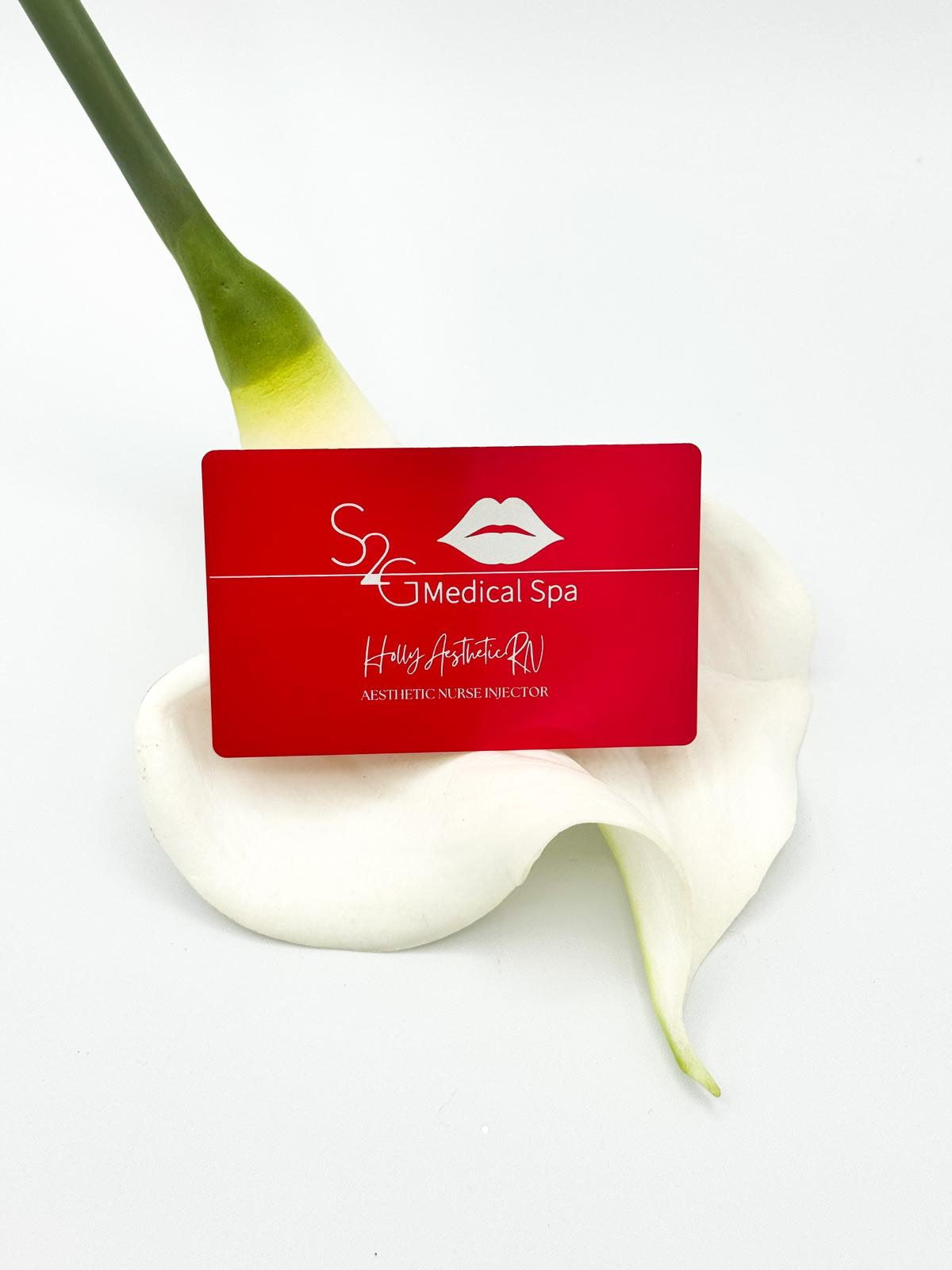 A red rectangular card for 'S2 Medical Spa' with white text and a lips logo, placed on a white calla lily flower against a clean white background.